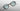 A pair of round eyeglasses with a black frame, light blue-green lenses, and gold metal accents, shown floating against a gray gradient background.
